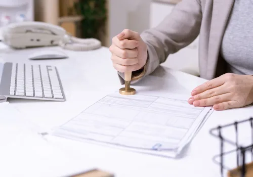 Hands of young female office worker sitting by desk and putting seal on financial document before sending it to client